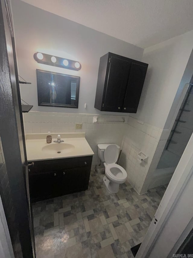 bathroom featuring vanity, toilet, tile walls, and a textured ceiling