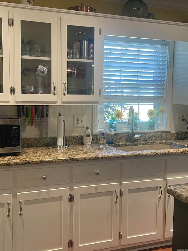 kitchen with white cabinets, decorative backsplash, light stone counters, and sink