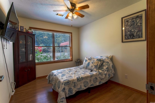 bedroom with ceiling fan, a textured ceiling, and dark hardwood / wood-style flooring