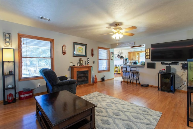 living room featuring a textured ceiling, ceiling fan, and light hardwood / wood-style flooring