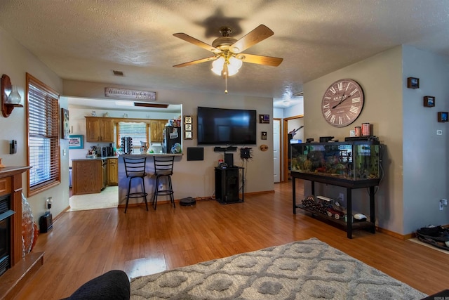 living room with light hardwood / wood-style floors, ceiling fan, and a textured ceiling