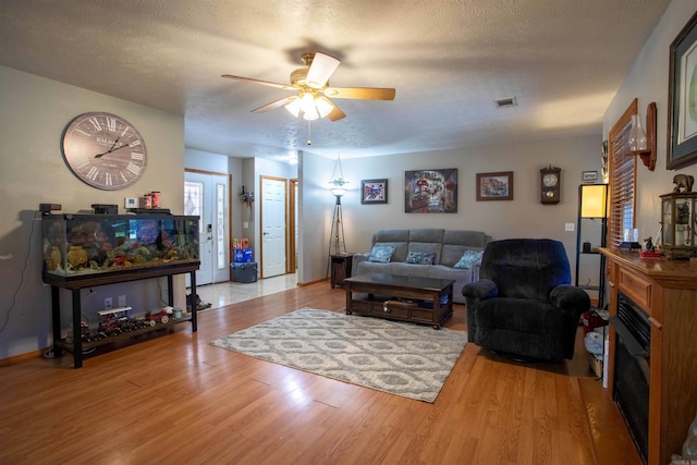 living room featuring ceiling fan, a textured ceiling, and light wood-type flooring