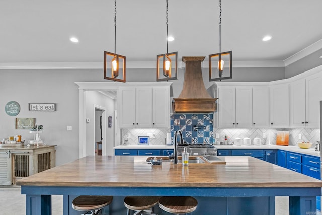 kitchen featuring decorative light fixtures, white cabinets, custom range hood, decorative backsplash, and a center island with sink