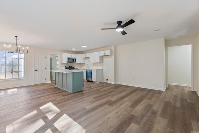 kitchen with appliances with stainless steel finishes, a kitchen island, white cabinetry, pendant lighting, and light hardwood / wood-style flooring