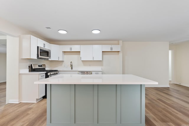 kitchen featuring white cabinets, a kitchen island, appliances with stainless steel finishes, light wood-type flooring, and sink