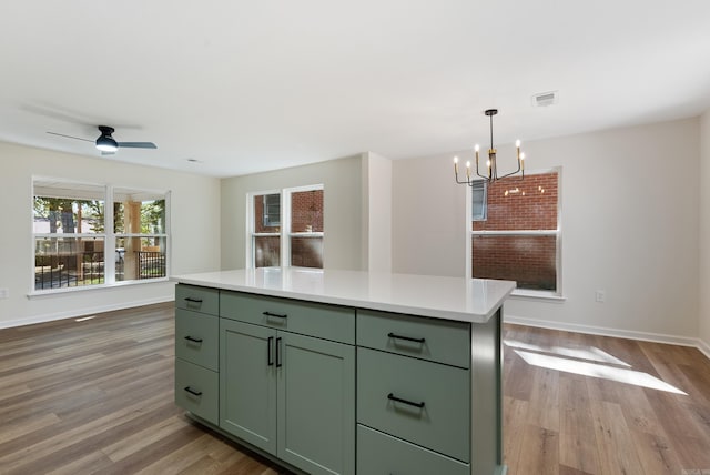 kitchen with light hardwood / wood-style floors, green cabinetry, ceiling fan with notable chandelier, and a kitchen island