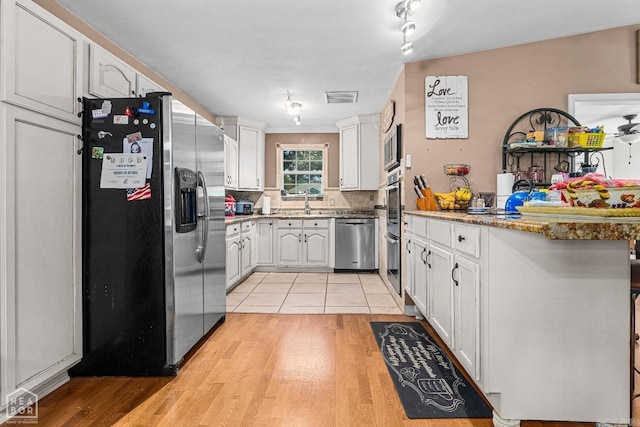 kitchen featuring stainless steel appliances, light hardwood / wood-style flooring, dark stone countertops, decorative backsplash, and white cabinets