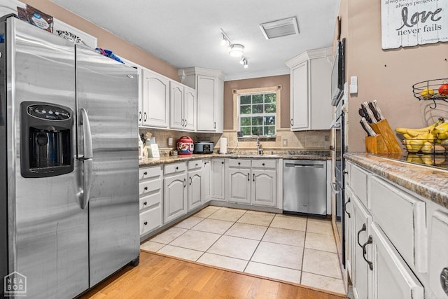 kitchen featuring sink, light tile patterned floors, backsplash, white cabinets, and appliances with stainless steel finishes