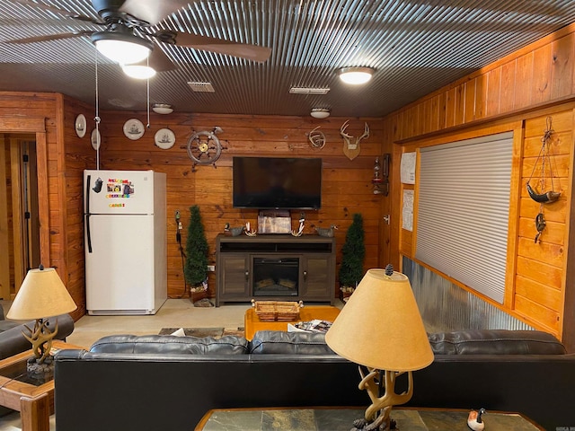 carpeted living room with ceiling fan, a fireplace, and wood walls