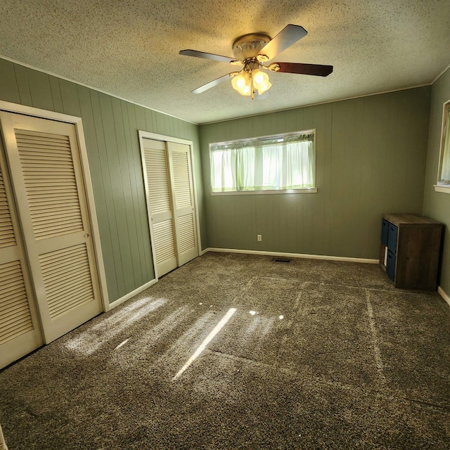 unfurnished bedroom featuring wooden walls, a textured ceiling, dark colored carpet, and ceiling fan