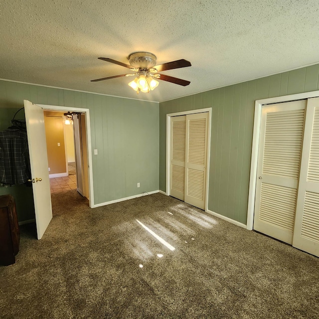 unfurnished bedroom featuring multiple closets, a textured ceiling, dark carpet, and ceiling fan