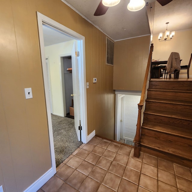 staircase featuring crown molding, ceiling fan with notable chandelier, wooden walls, and tile patterned floors