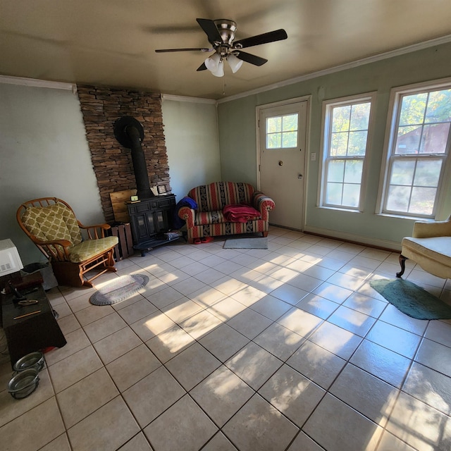 living room featuring a wood stove, ceiling fan, crown molding, and light tile patterned floors