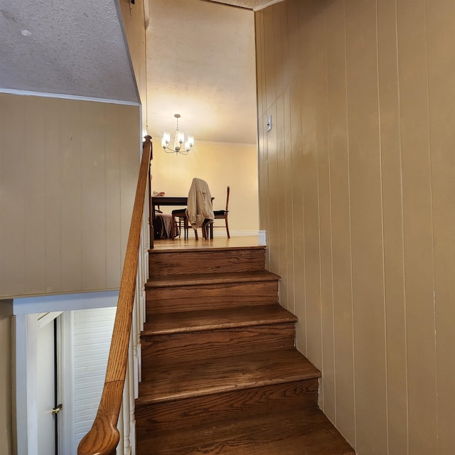 stairs with a textured ceiling, wooden walls, and an inviting chandelier