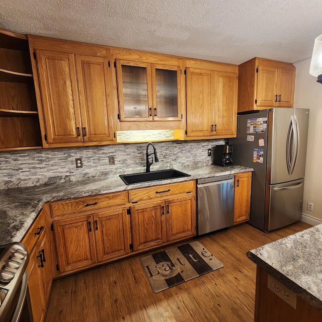 kitchen featuring tasteful backsplash, appliances with stainless steel finishes, a textured ceiling, sink, and light hardwood / wood-style flooring