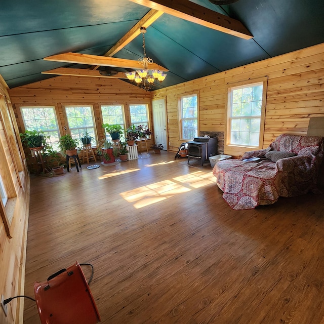 living room featuring lofted ceiling with beams, wood-type flooring, a wood stove, a notable chandelier, and wood walls