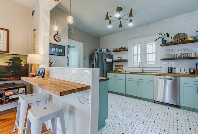 kitchen with sink, butcher block countertops, stainless steel appliances, decorative light fixtures, and a breakfast bar area