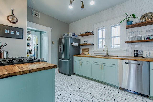 kitchen with wood counters, appliances with stainless steel finishes, sink, and tasteful backsplash