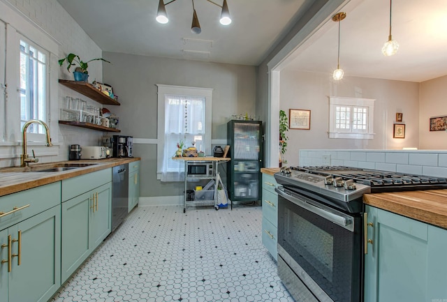 kitchen featuring black dishwasher, sink, gas stove, wood counters, and decorative light fixtures