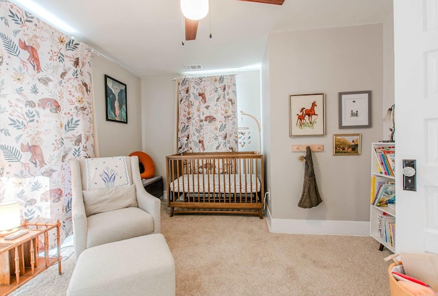 carpeted bedroom featuring a nursery area and ceiling fan