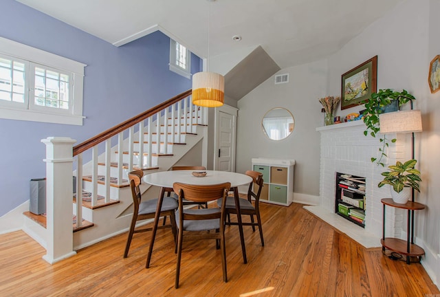 dining room featuring vaulted ceiling, light wood-type flooring, and a fireplace