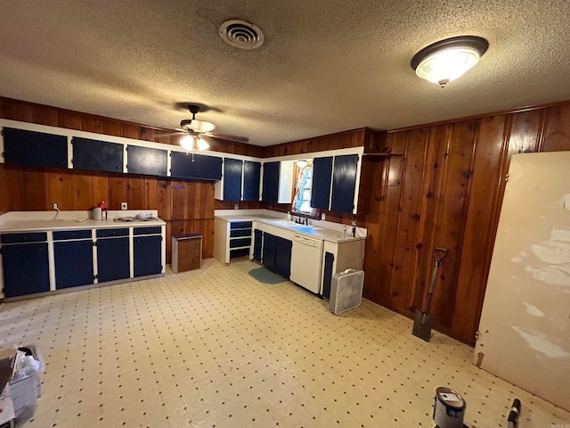 kitchen with a textured ceiling, wooden walls, white dishwasher, and sink