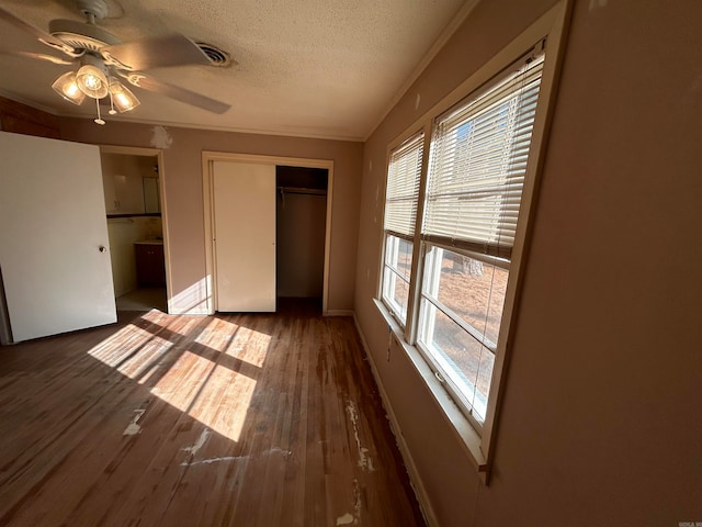 unfurnished bedroom with a closet, dark wood-type flooring, crown molding, a textured ceiling, and ceiling fan