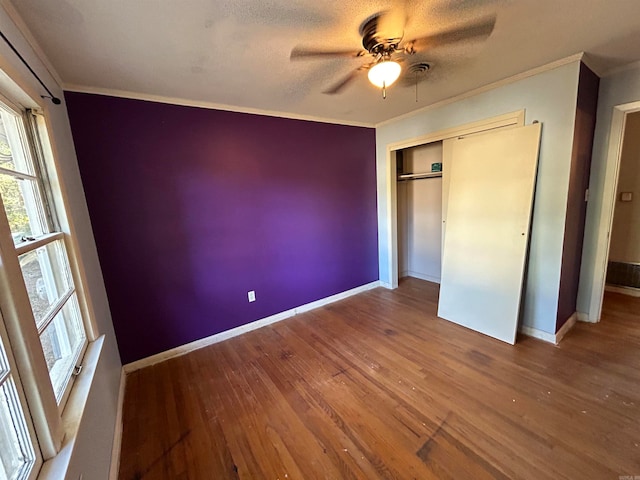 unfurnished bedroom with a textured ceiling, a closet, ceiling fan, crown molding, and hardwood / wood-style flooring