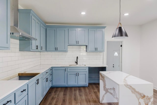 kitchen featuring wall chimney range hood, backsplash, dark hardwood / wood-style floors, sink, and decorative light fixtures