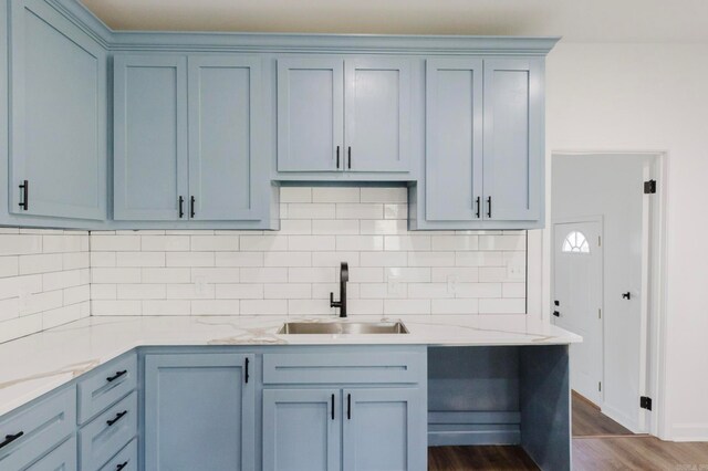 kitchen featuring hardwood / wood-style floors, sink, blue cabinetry, light stone counters, and tasteful backsplash