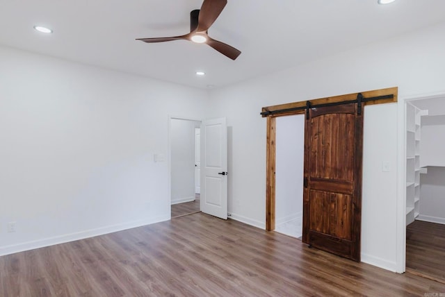 unfurnished bedroom featuring a walk in closet, ceiling fan, a barn door, hardwood / wood-style flooring, and a closet