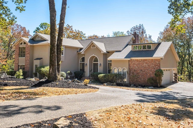 view of front of house featuring a garage, brick siding, a shingled roof, driveway, and a chimney