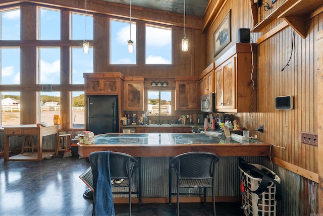 kitchen featuring hanging light fixtures, black fridge, high vaulted ceiling, a wealth of natural light, and wooden walls