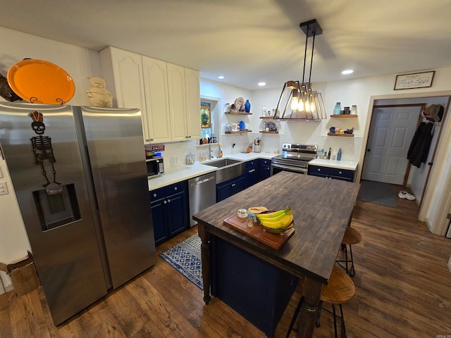 kitchen featuring appliances with stainless steel finishes, pendant lighting, white cabinets, dark wood-type flooring, and blue cabinetry