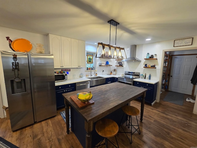 kitchen featuring wall chimney range hood, white cabinets, pendant lighting, blue cabinets, and appliances with stainless steel finishes