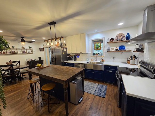 kitchen featuring wall chimney range hood, dark hardwood / wood-style floors, stainless steel appliances, sink, and blue cabinets