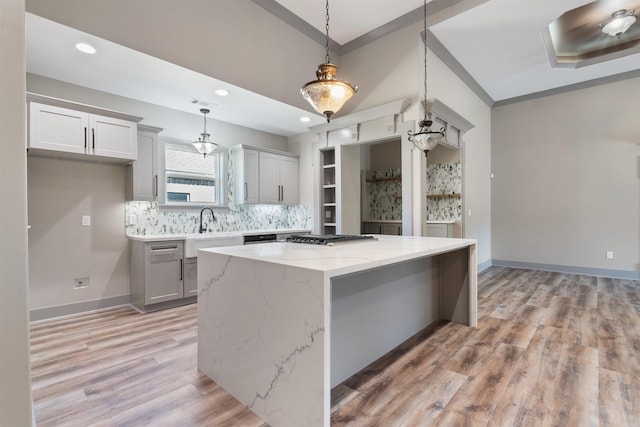 kitchen with a kitchen island, hanging light fixtures, ornamental molding, light stone countertops, and light hardwood / wood-style floors