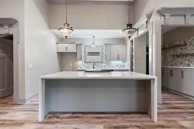 kitchen with sink, a kitchen island, decorative light fixtures, decorative backsplash, and light hardwood / wood-style flooring