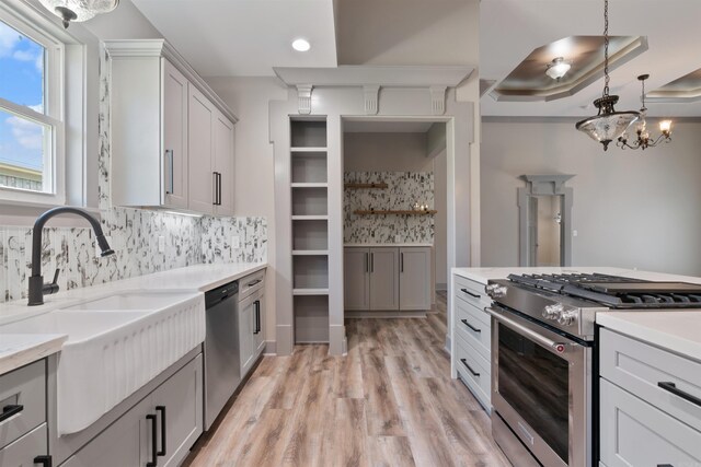 kitchen featuring hanging light fixtures, a tray ceiling, sink, appliances with stainless steel finishes, and light hardwood / wood-style floors