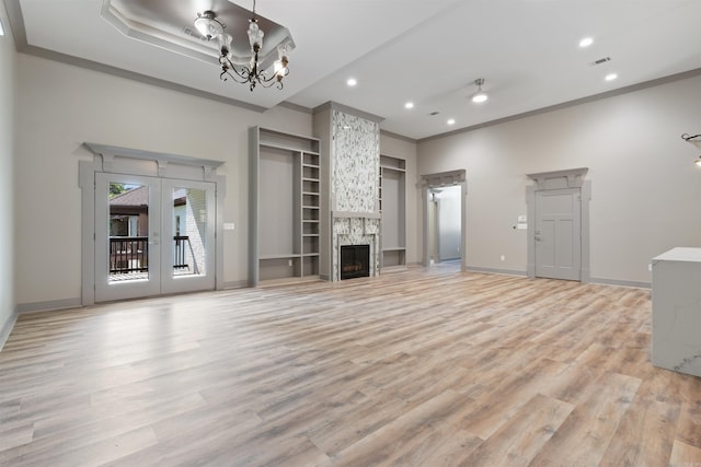 unfurnished living room with ornamental molding, french doors, a stone fireplace, and light hardwood / wood-style floors