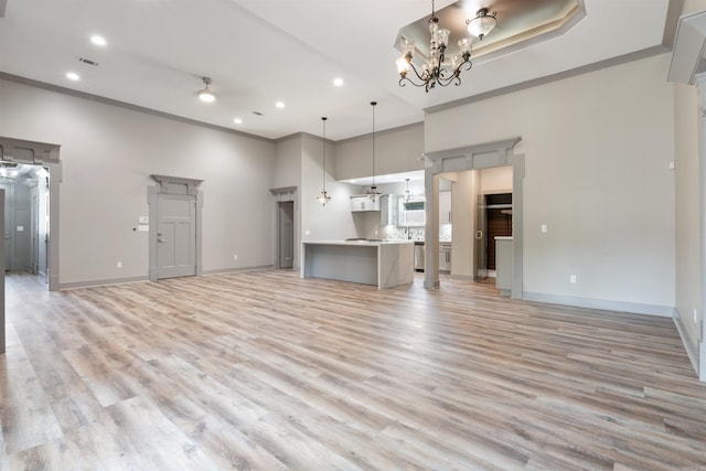 unfurnished living room featuring a towering ceiling, crown molding, light hardwood / wood-style flooring, and a chandelier