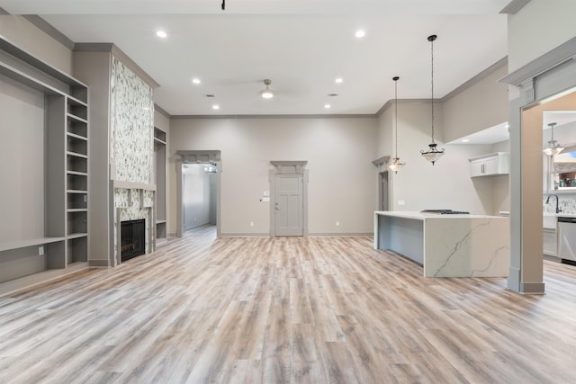 unfurnished living room with a large fireplace, ornamental molding, a high ceiling, and light wood-type flooring