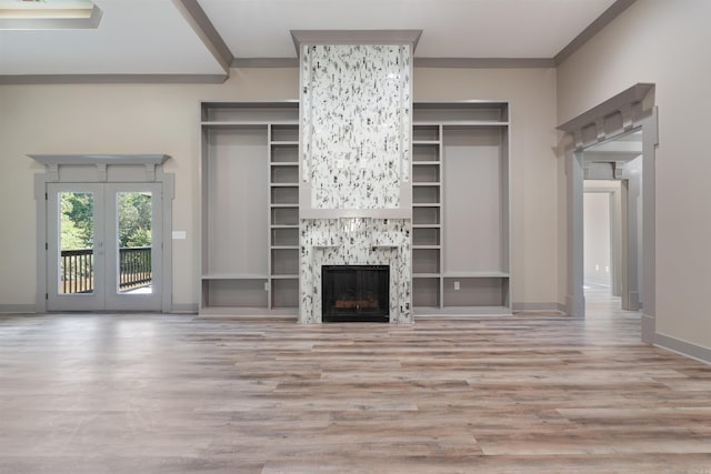 unfurnished living room featuring a stone fireplace, french doors, ornamental molding, and light wood-type flooring