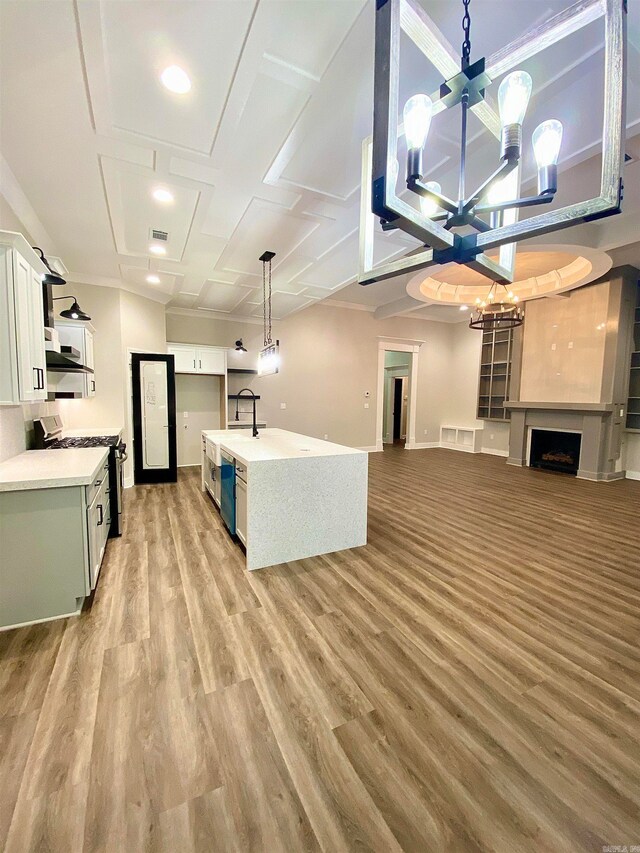 kitchen featuring white cabinets, an island with sink, light wood-type flooring, range, and sink