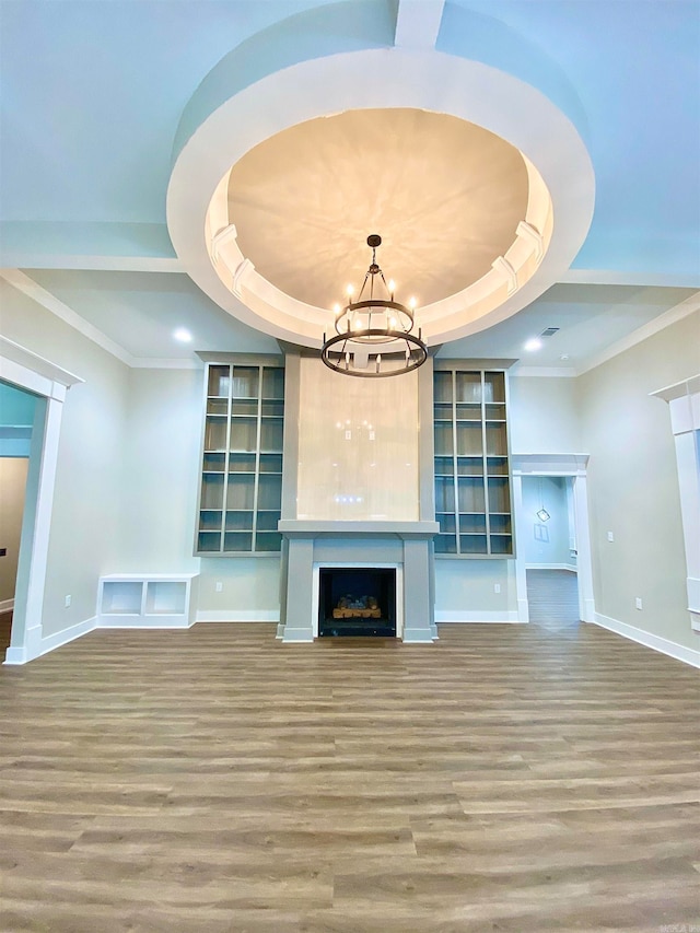 unfurnished living room with ornamental molding, a notable chandelier, hardwood / wood-style floors, and a tray ceiling