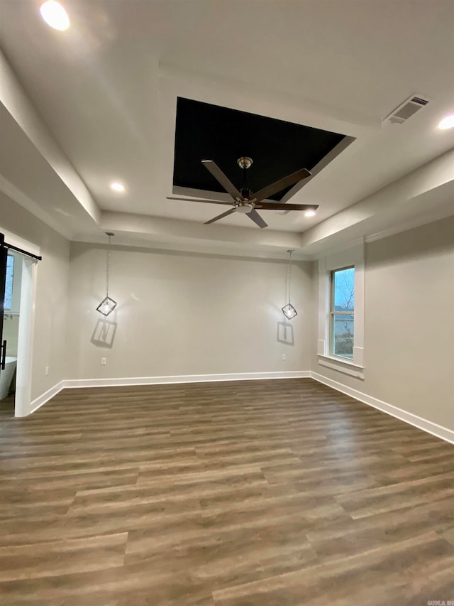 empty room with ceiling fan, a raised ceiling, a barn door, and hardwood / wood-style floors