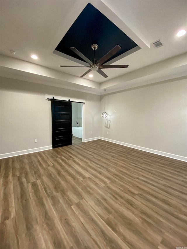 empty room featuring ceiling fan, a barn door, and hardwood / wood-style floors