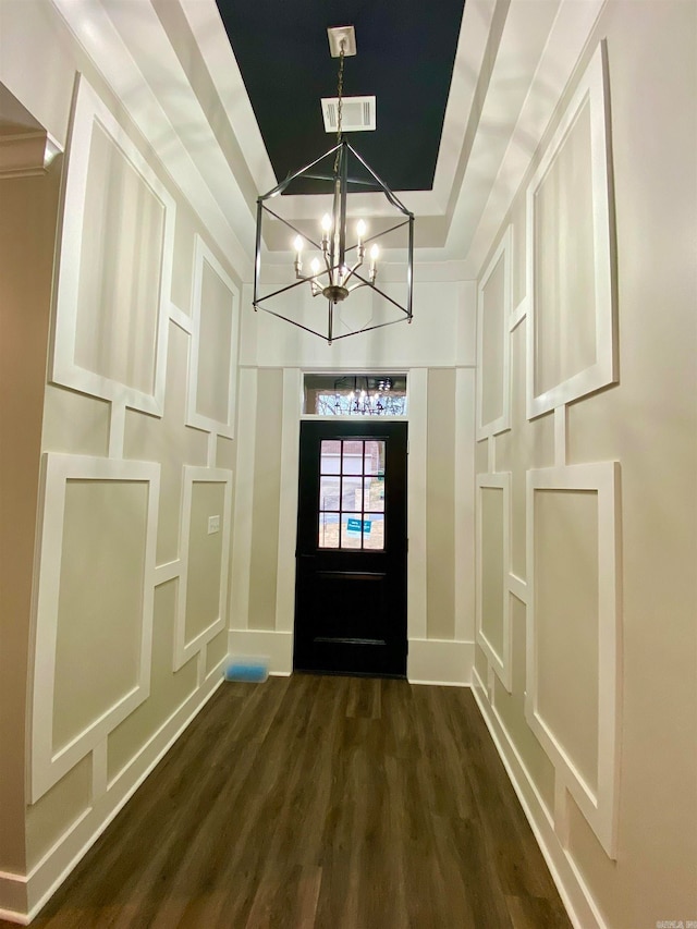 doorway to outside with dark wood-type flooring, a tray ceiling, and an inviting chandelier