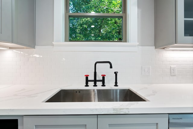 kitchen with sink, light stone counters, gray cabinetry, and backsplash