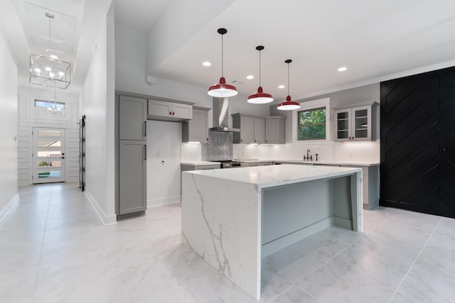 kitchen with a kitchen island, wall chimney range hood, sink, gray cabinets, and light stone counters